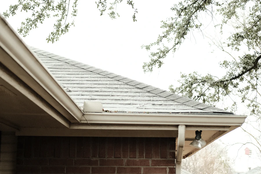 Brick house roofline with a white gutter under overhanging branches